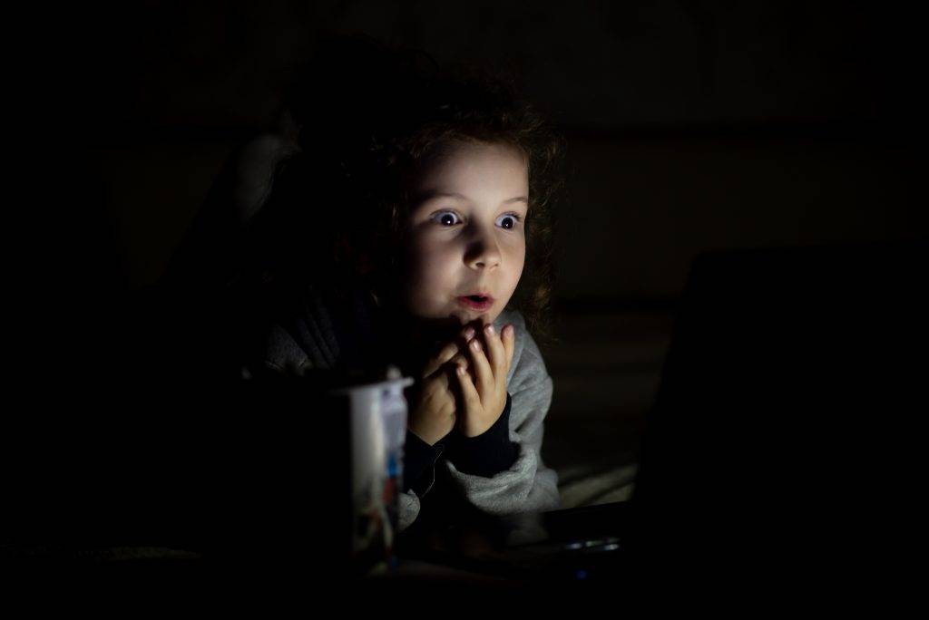 A girl watches cartoons in the dark. She's at home. Childhood. Leisure.
